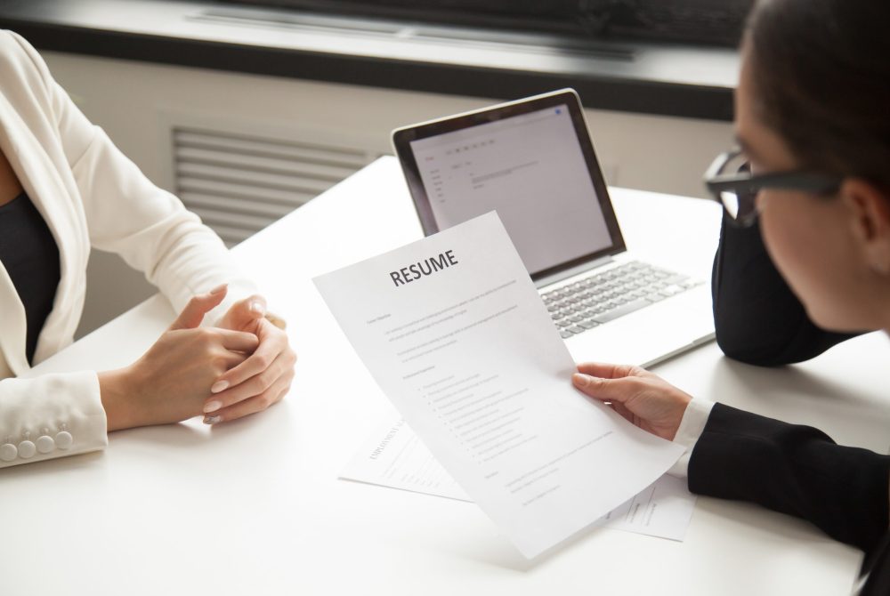 Company CEO and HR manager reading applicant resume or cv while employee waiting for questions, discussion and result during recruitment process in office. Concept of hiring, employment. Close up view